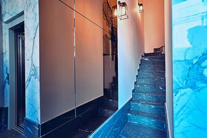 Uma escadaria de mármore com corrimão, luminária e uma porta no topo.