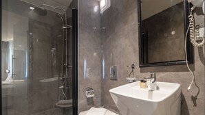 Un baño moderno con cabina de ducha de vidrio, lavabo blanco y un espejo grande.