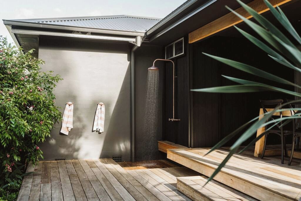 A modern outdoor shower area with a wooden deck and a metal roof.