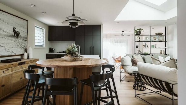 A modern kitchen with a central island, bar stools, and a dining area with a sofa and chairs. - Dunes on Sandy Wha (Gerringong)