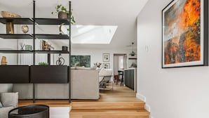 A modern living room with a sofa, a black coffee table, and a black basket. There is a skylight above the sofa and a painting on the wall. - Dunes on Sandy Wha (Gerringong)