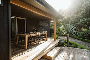 Una terraza de madera con una mesa y sillas, rodeada de vegetación y un sendero.