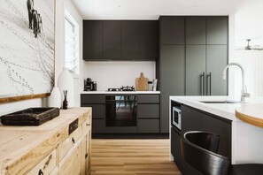A modern kitchen with dark cabinets, a wooden countertop, and a built-in oven. - Dunes on Sandy Wha (Gerringong)