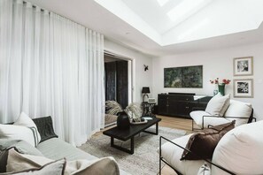 A modern living room with a sofa, a coffee table, and a TV. There is a painting on the wall and a window with curtains. - Dunes on Sandy Wha (Gerringong)