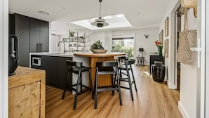 A modern kitchen with a central island, black bar stools, and a skylight. - Dunes on Sandy Wha (Gerringong)