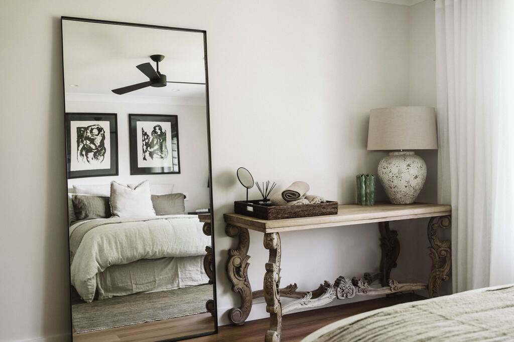 A bedroom with a bed, a bedside table with a lamp, a mirror, and framed artwork on the wall.