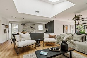A modern living room with a skylight, a sofa set, a coffee table, and a kitchen in the background. - Dunes on Sandy Wha (Gerringong)