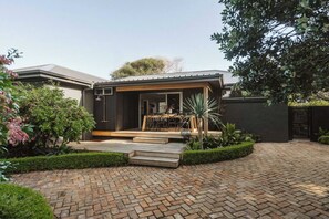 A modern house with a paved driveway, a wooden deck, and a well-maintained garden. - Dunes on Sandy Wha (Gerringong)