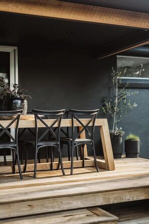 An outdoor dining area with a wooden table and chairs, potted plants, and a view of the surrounding area. - Dunes on Sandy Wha (Gerringong)