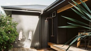 A modern outdoor shower area with a wooden deck and a metal roof. - Dunes on Sandy Wha (Gerringong)