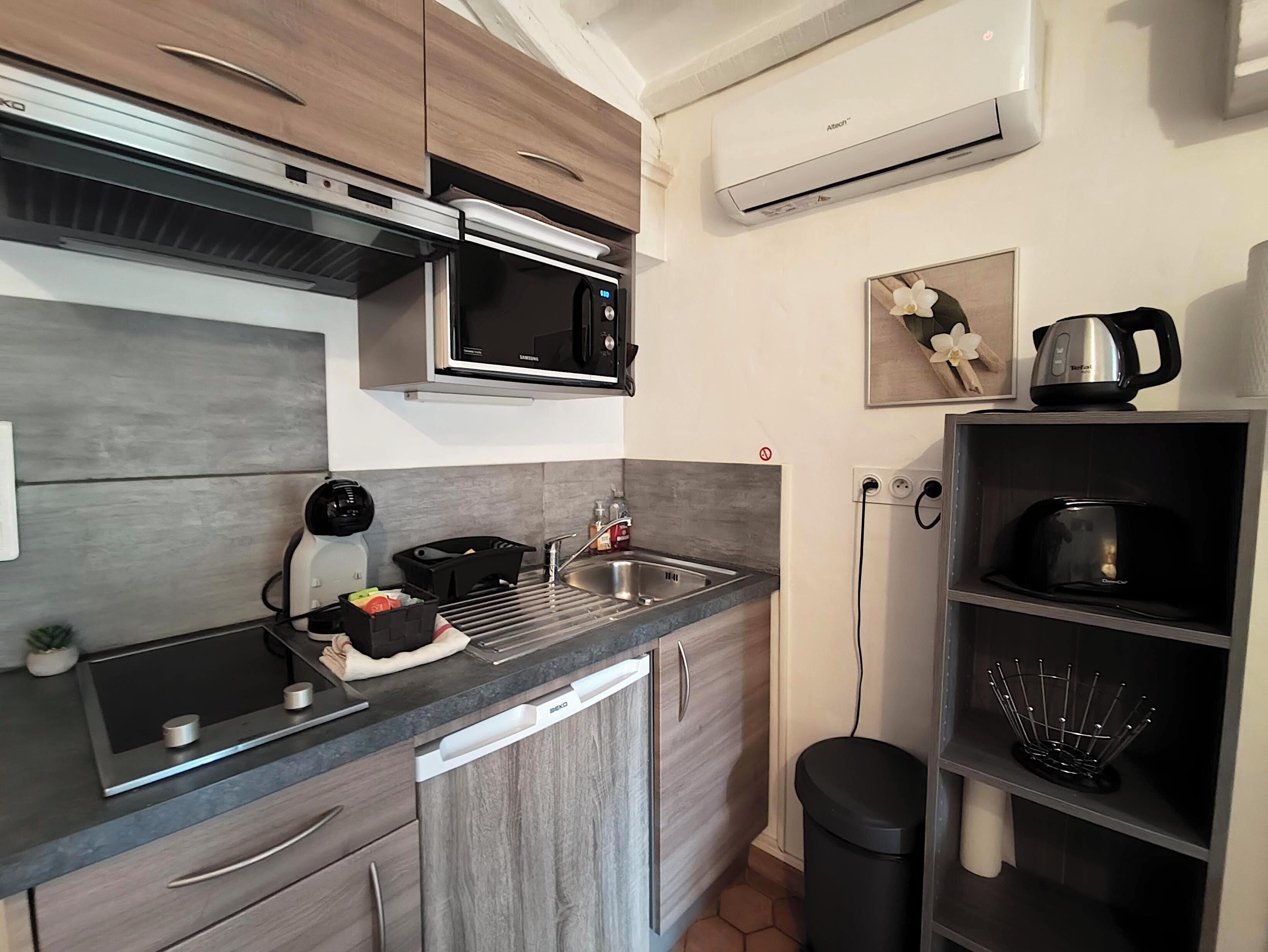A compact kitchen with a microwave, sink, and a kettle on the countertop.