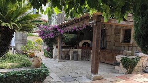 Une terrasse en pierre avec une pergola, des sièges d’extérieur et un four en pierre.