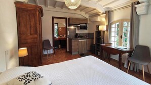 Une chambre à coucher comprenant un lit, une chaise, un bureau, une lampe et donnant sur une cuisine et une salle de bain.