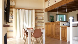 Un comedor con mesa y sillas, armarios de madera y una zona de cocina con encimera y electrodomésticos.