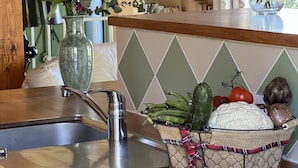 Una cocina con un lavamanos de acero inoxidable, una estufa a gas, una cesta de frutas y un florero con flores sobre la encimera.