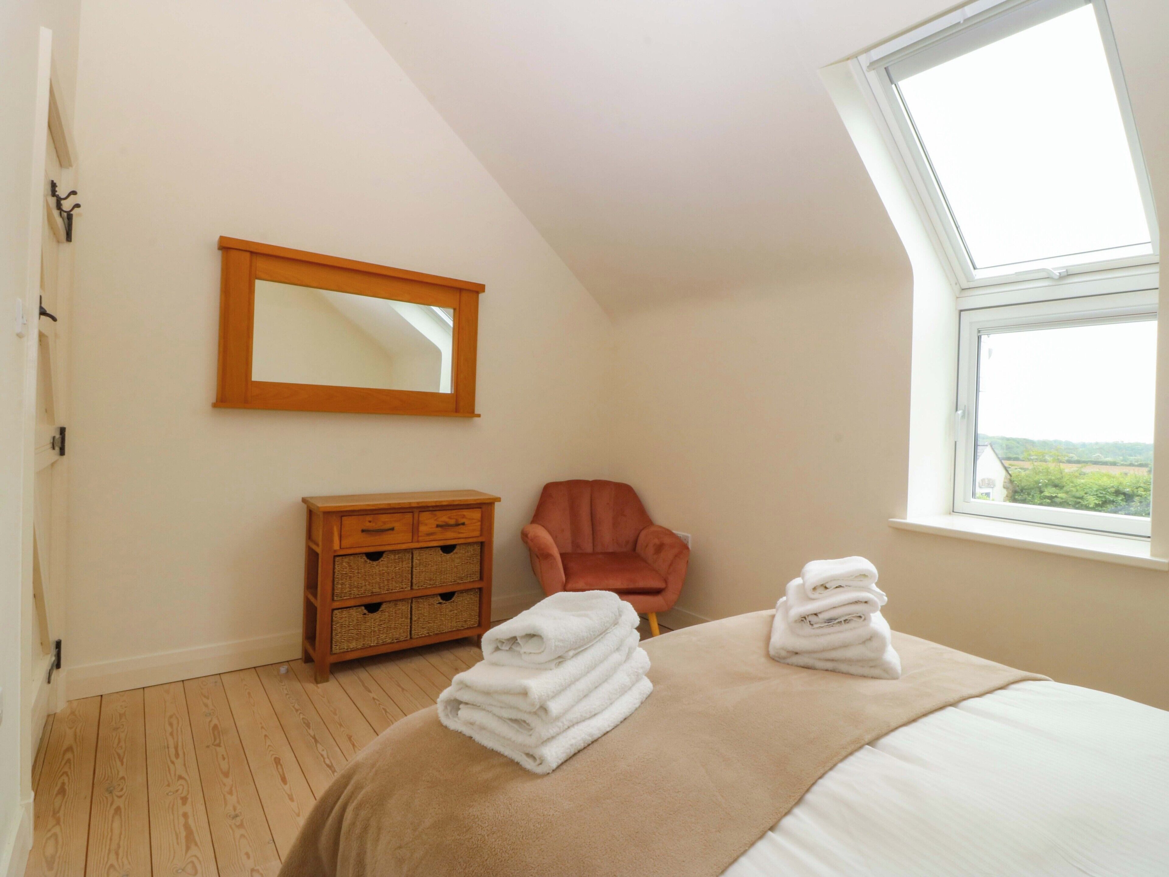 A bedroom with a bed, a chair, a wooden dresser, a mirror, and a window with a view.