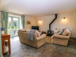 A living room with a sofa, armchairs, a television, a fireplace, and a door leading outside.