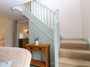 A staircase with a light blue handrail and beige carpeted steps, a wooden table with a vase of flowers, and a beige sofa with a pillow.