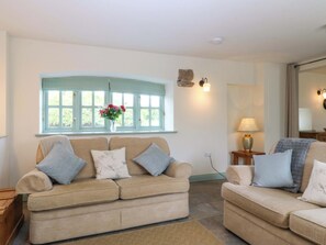 A living room with two beige sofas, a window with a view, a vase with flowers, and a lamp on a side table.
