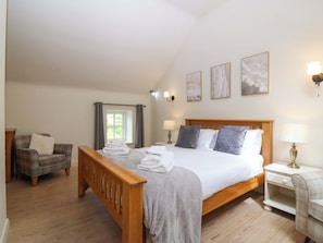 Ein Schlafzimmer mit einem hölzernen Bett, einem Sessel, einem Nachttisch und einem Fenster mit Vorhängen.