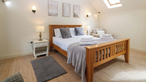 Un dormitorio con cama de madera, mesitas de noche, un banco, alfombra gris y un tragaluz.