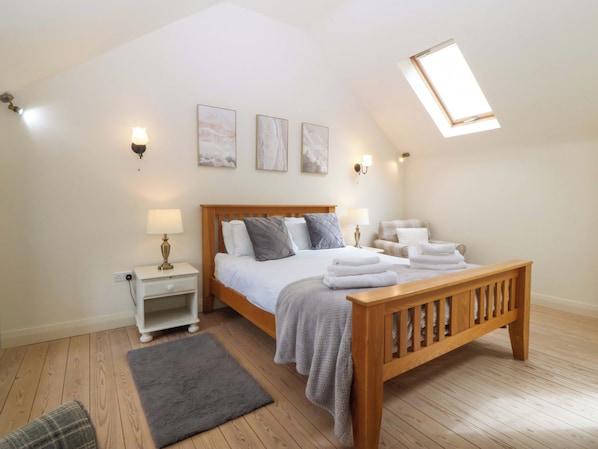 A bedroom with a wooden bed, bedside tables, a bench, a grey rug, and a skylight.