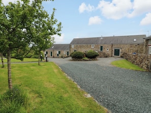 A stone building with a gravel driveway, green doors, and a grassy area with trees.
