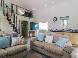 A spacious living area with a sofa set, a staircase, a kitchen, and a dining area.