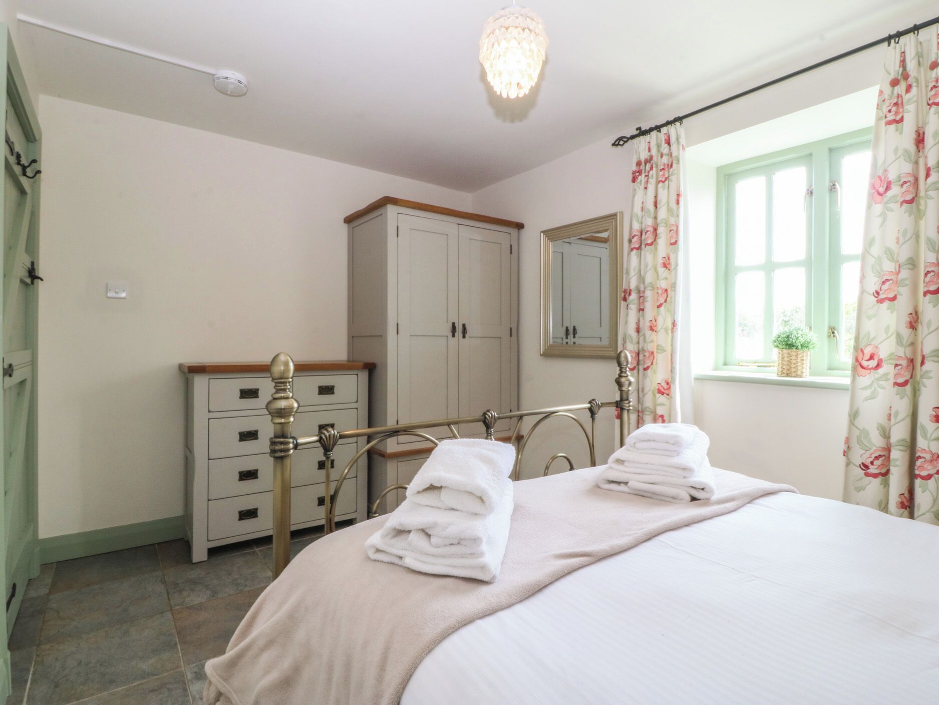 Um quarto com cama, penteadeira, espelho e janela com cortinas.