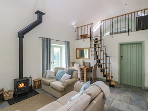 A cozy living room with a sofa, a table, a staircase, and a green door.