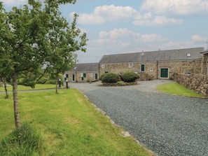 A stone building with a gravel driveway and green doorways, surrounded by grass and trees.