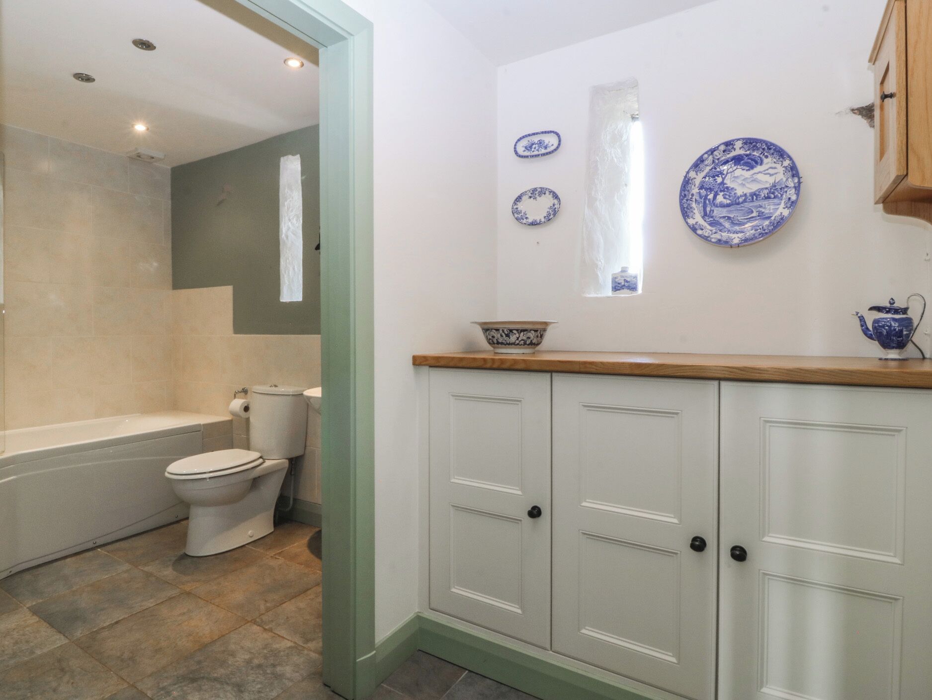 A bathroom with a bathtub, toilet, and a sink area with decorative plates.