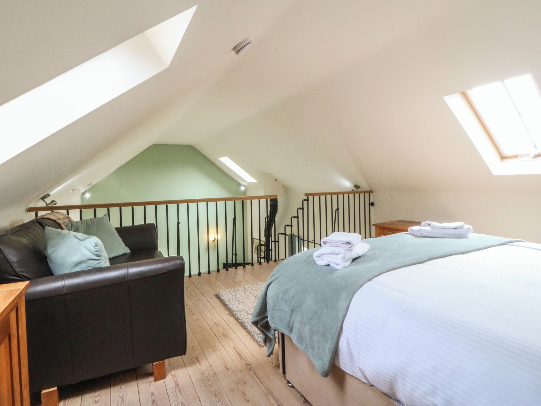 A bedroom with a sloped ceiling, a bed, a sofa, and a staircase.