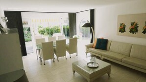 A modern living room with a sofa, coffee table, and chairs. There is a large window with a view of greenery outside.