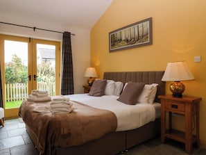 A bedroom with a bed, two bedside tables with lamps, a painting on the wall, and a view through a door. - No 3 The Dairy (Llangefni)