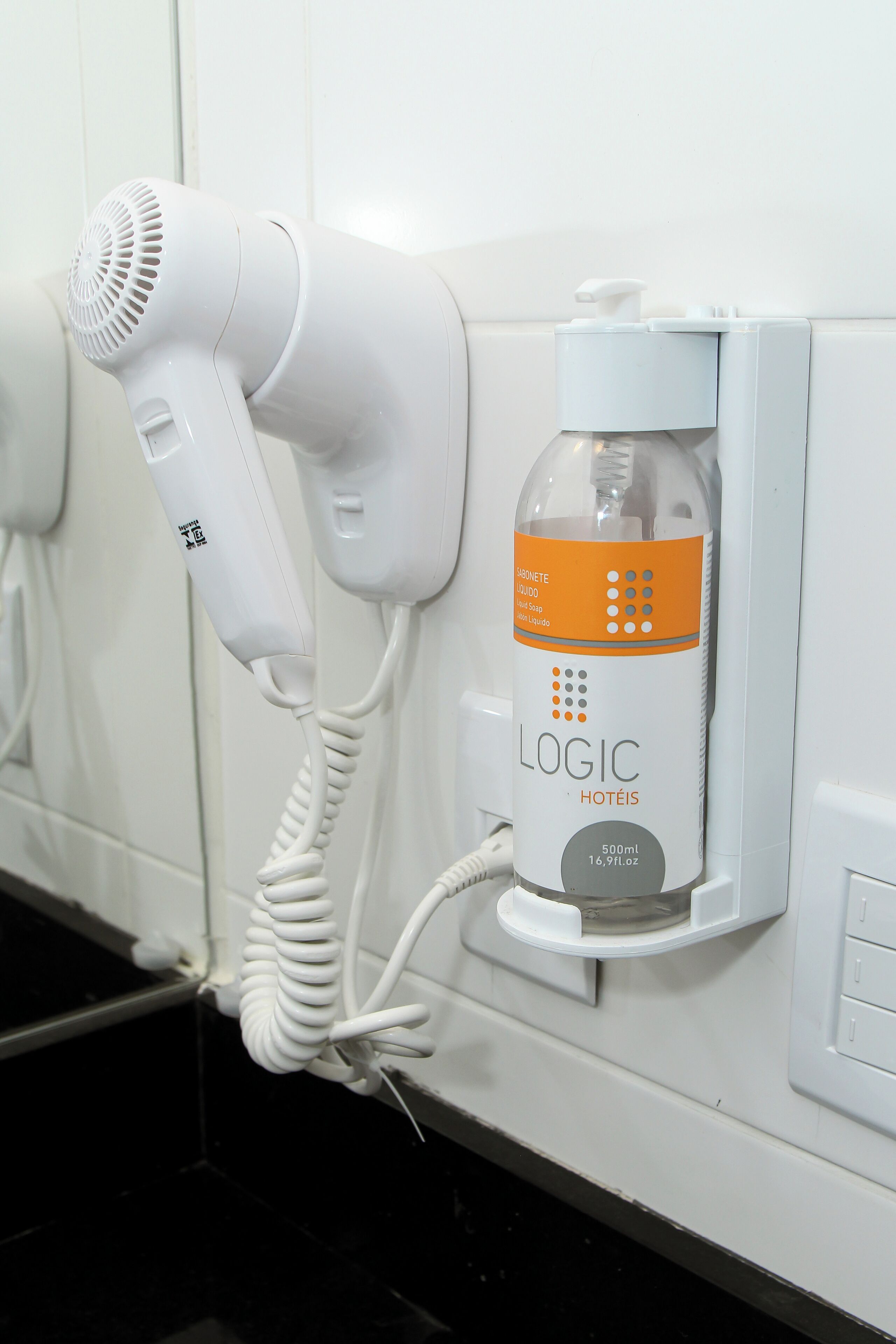 A hair dryer and a bottle of liquid soap attached to a wall.