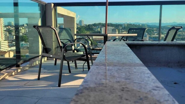 Una terraza en la azotea con una mesa larga y sillas, un paraguas grande y vistas a la ciudad.