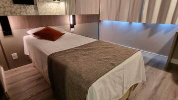 A hotel room with a bed, a wall-mounted TV, an air conditioning unit, and a window with curtains.