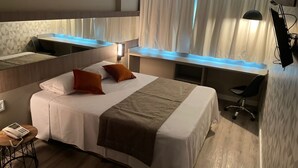 Una habitación de hotel moderna con una cama grande, un escritorio y una silla. Hay un teléfono sobre una mesita y una ventana con cortinas.