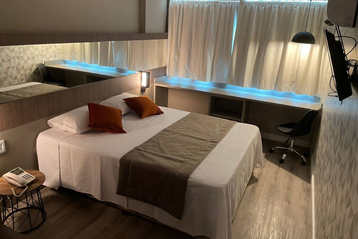 Una habitación de hotel moderna con una cama grande, un escritorio y una silla. Hay un teléfono sobre una mesita y una ventana con cortinas.