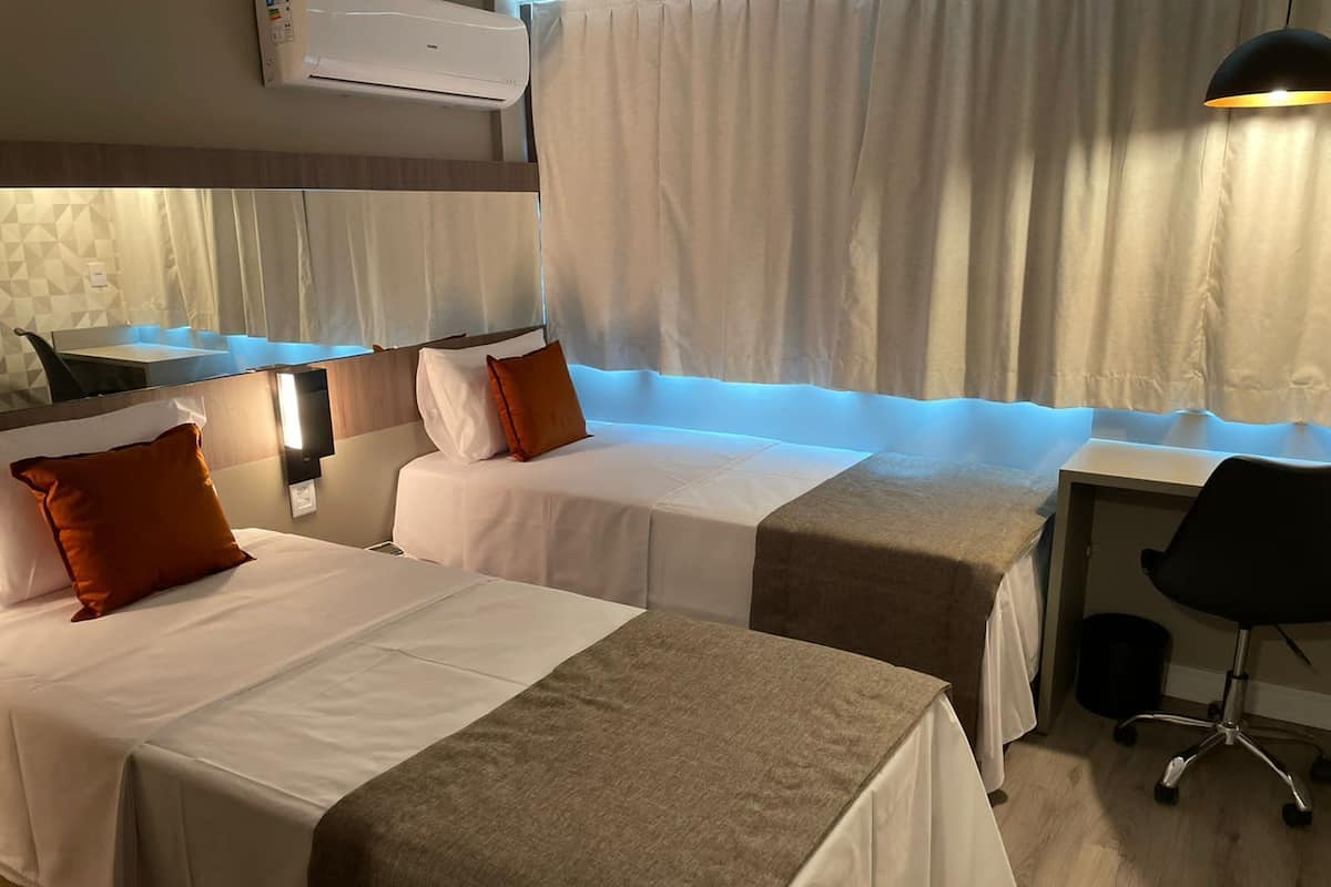 Habitación de hotel con dos camas, un escritorio, una silla y una ventana con cortinas.