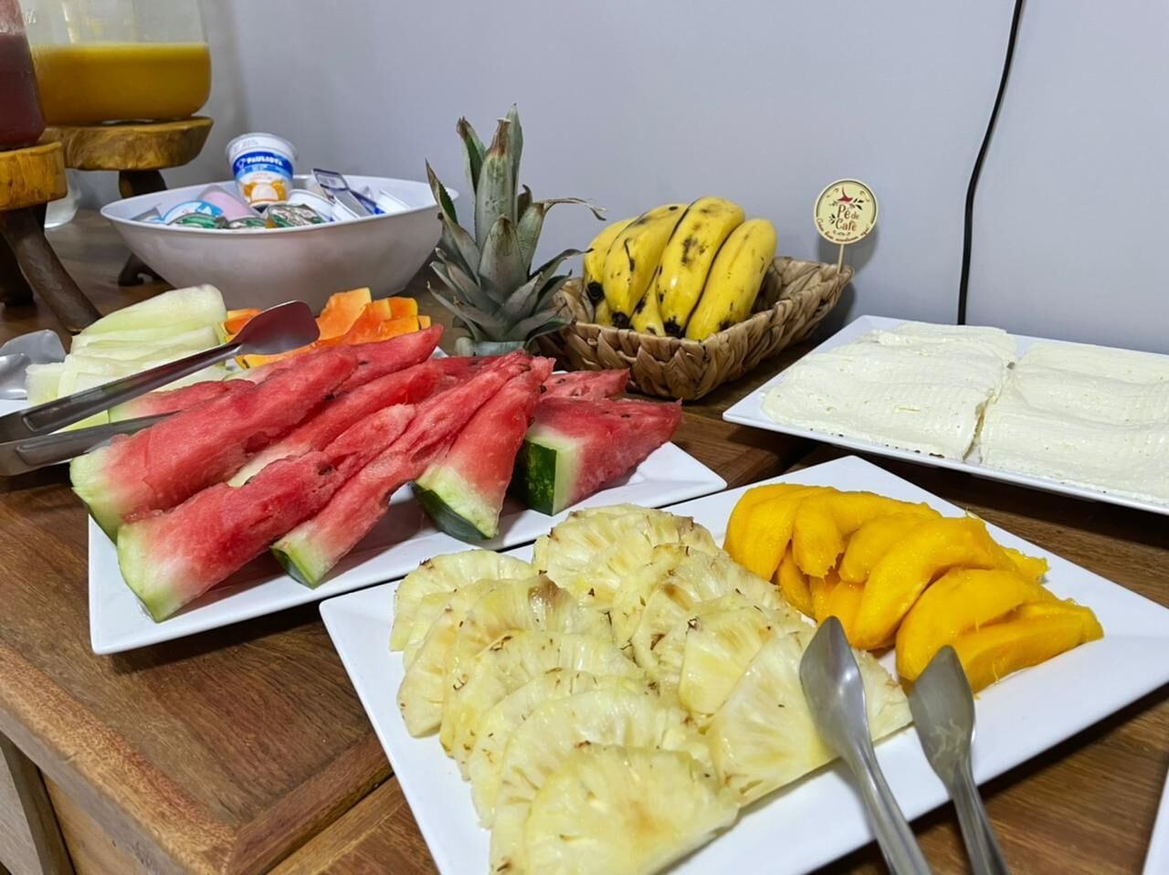 A breakfast table with plates of watermelon, pineapple, mango, and bananas.