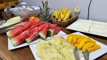A breakfast table with plates of watermelon, pineapple, mango, and bananas.