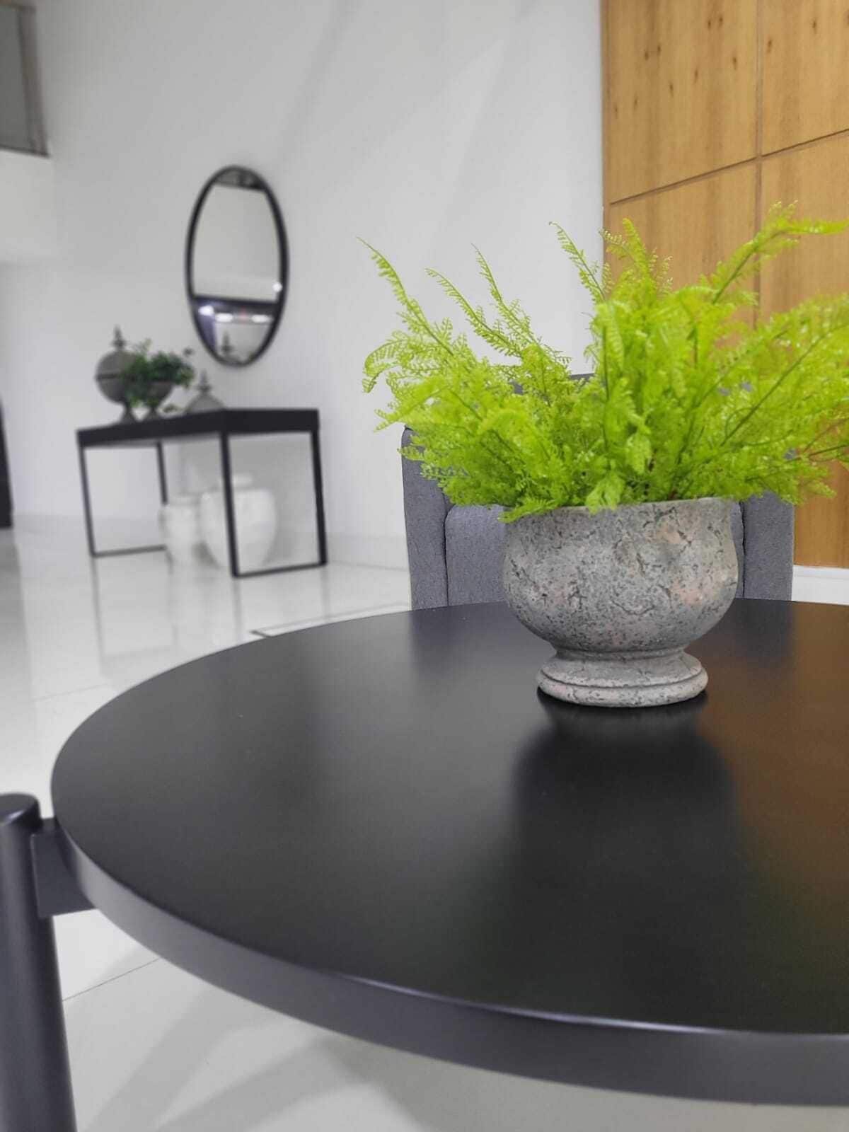 A round table with a grey stone planter containing green foliage. A black-framed mirror hangs on the wall above the table.