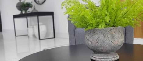 Una mesa redonda con una jardinera de piedra gris que contiene follaje verde. Un espejo con marco negro cuelga de la pared sobre la mesa.