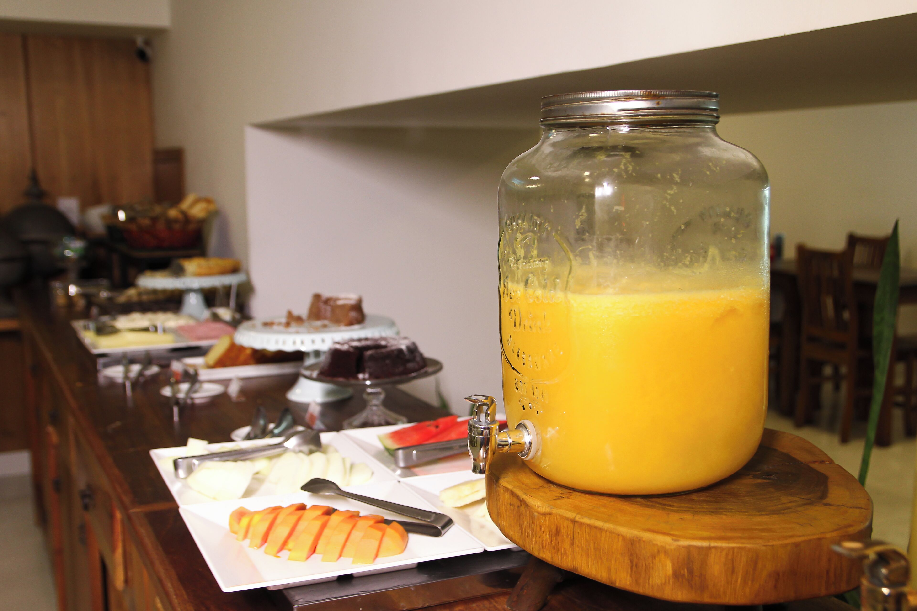 Ein Saftspender mit Holzfuß, einem Metallhahn und einem mit Orangensaft gefüllten Glasbehälter.