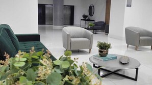 Un hall moderno con un sofá verde, dos sillones grises, una mesa de centro con una planta y un espejo en la pared.