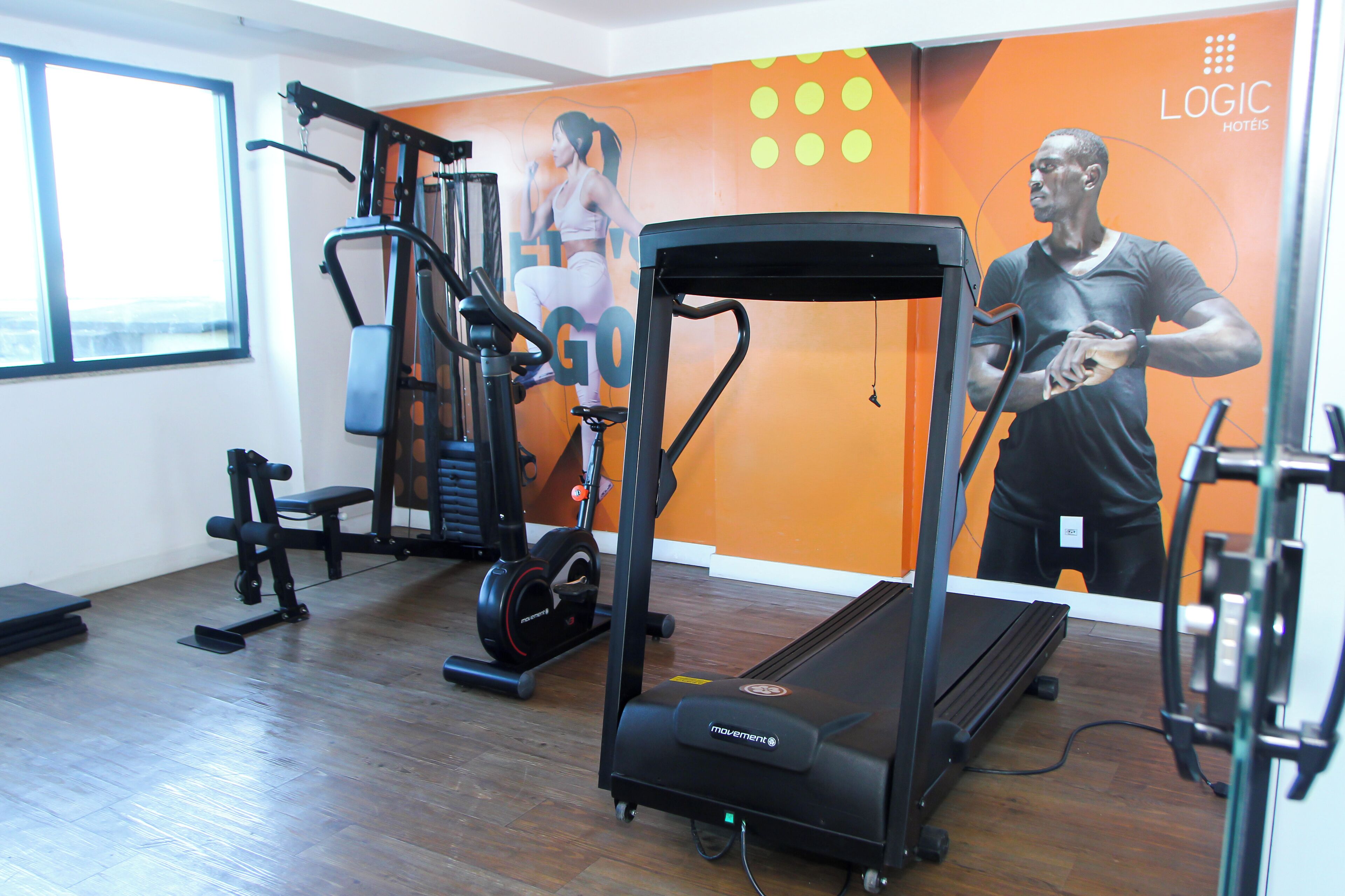Een sportschool met diverse fitnessapparaten, waaronder een loopband, een hometrainer en krachtapparaten.
