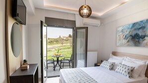 A modern bedroom with a large bed, a TV, a dining table with chairs, and a view of a garden. - Destino villa ,huge pool,Near Rethymno (Agios Markos)