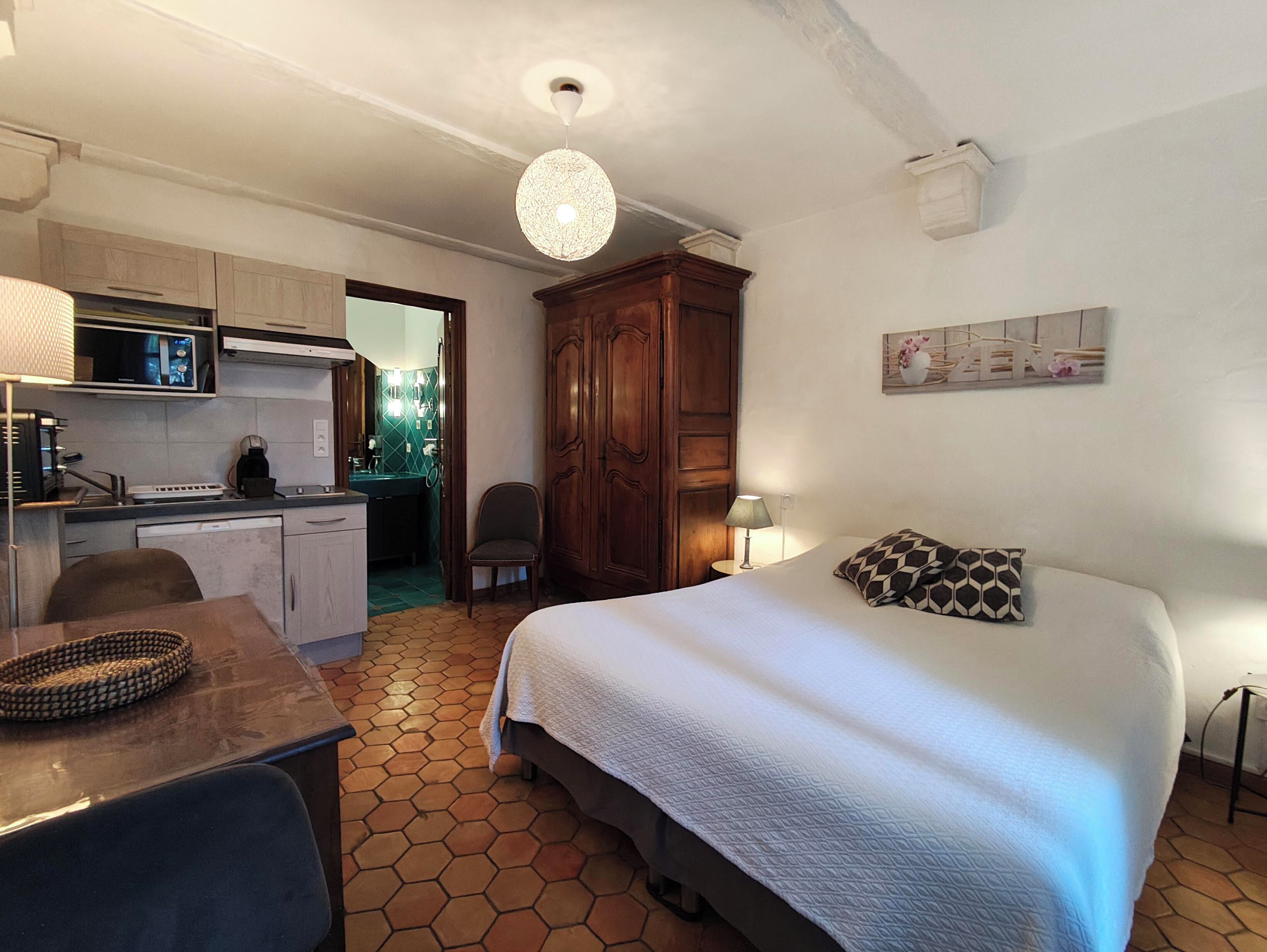 A bedroom with a bed, a desk, a chair, a wardrobe, and a kitchen area with a microwave.